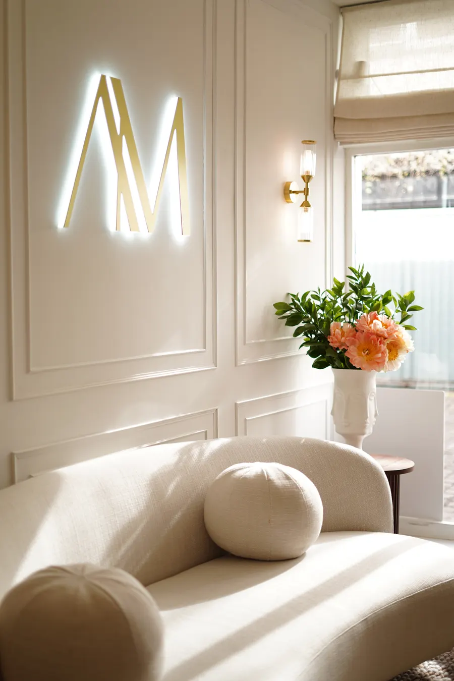 The Aesthetic by Maria clinic interior in Kensington — a cream bouclé chair, the gold monogram and fresh peonies